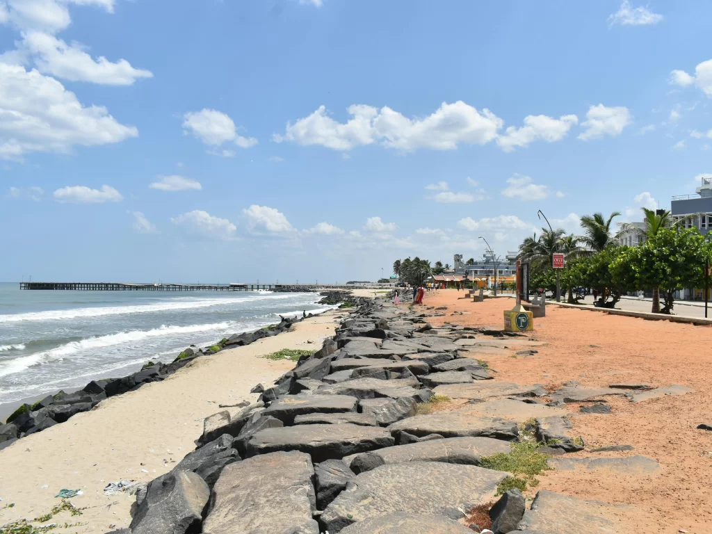 Promenade Beach at Puducherry during sunny day, featuring rocky shore pier and palm trees, perfect romantic experience Puducherry tour package.