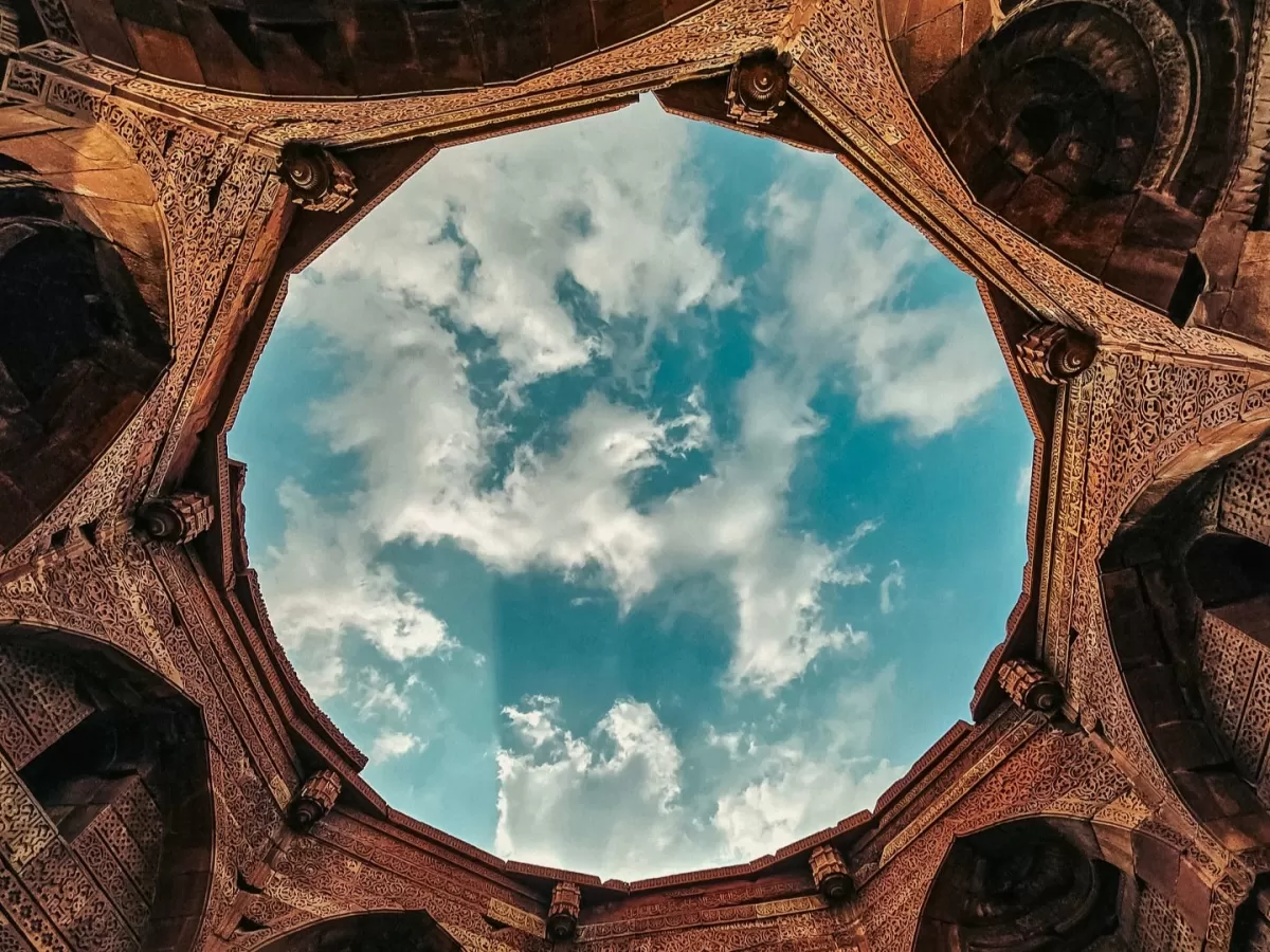 Qutub Minar complex upward view of ornate Indo-Islamic stone arch framing the blue sky and clouds, highlighting Delhi’s UNESCO World Heritage architecture and popular photography spot for Qutub Minar 