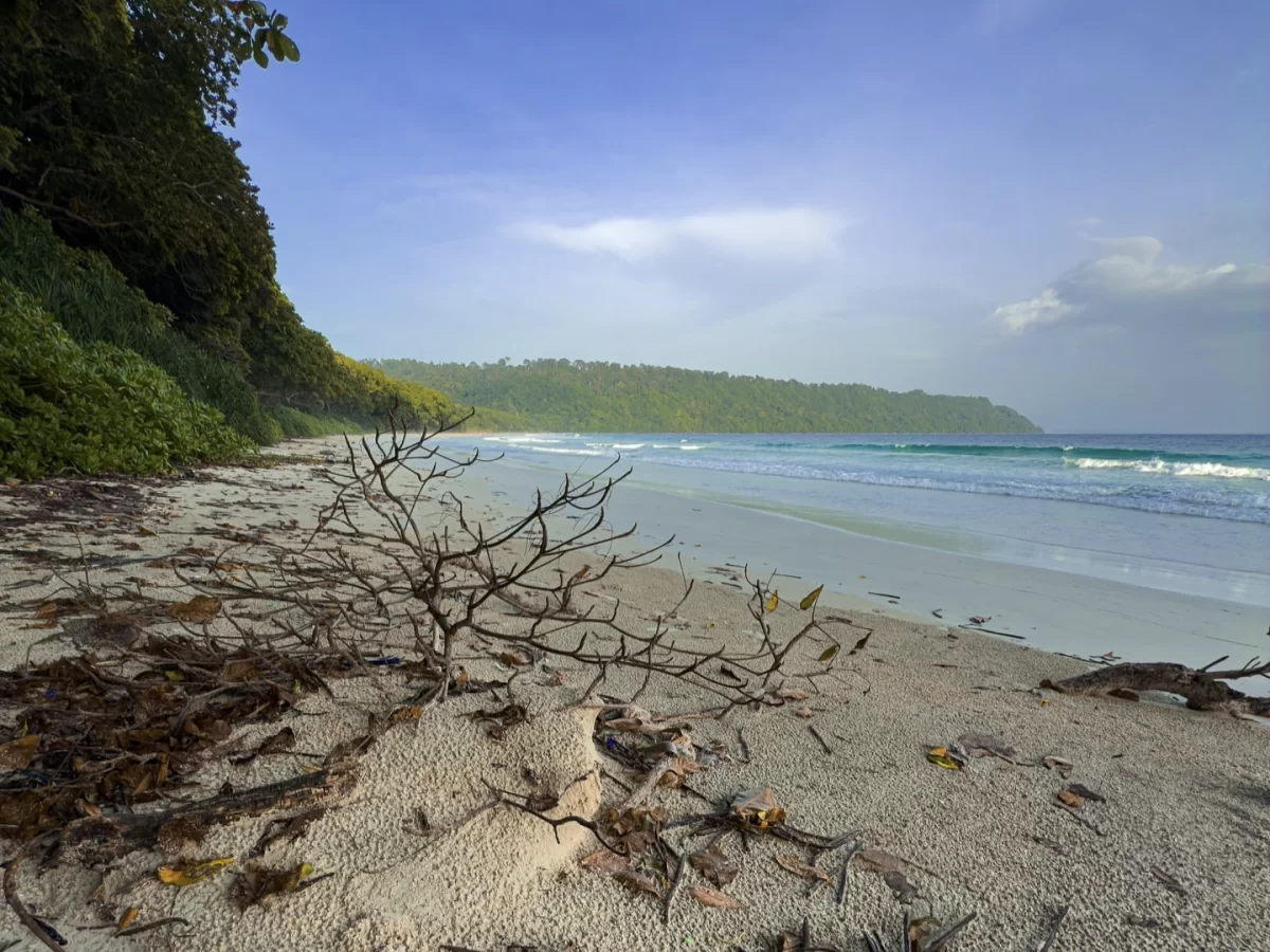 Radhanagar Beach Beach No.7 Havelock Island Andaman Nicobar during partly cloudy day, featuring pristine white sand, turquoise waves, lush forest backdrop, perfect tropical beach tour package.