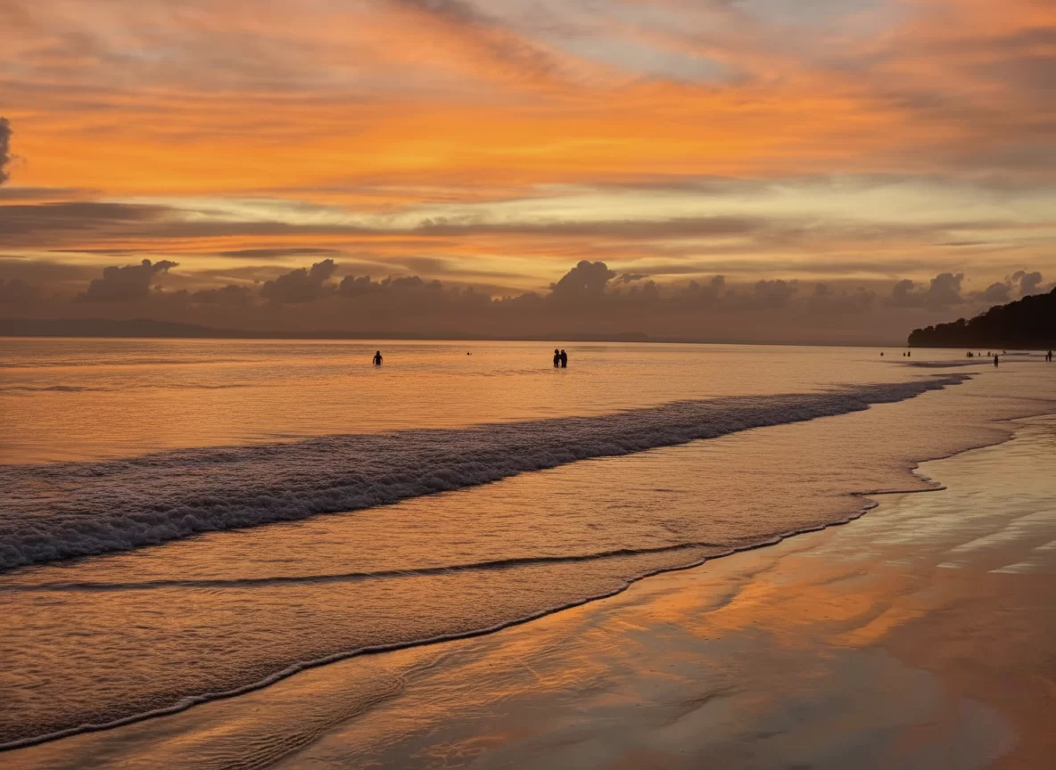 Radhanagar Beach No.7 Havelock Island Andaman sunset panorama with orange sky, featuring calm turquoise ocean waves, distant silhouettes of people, perfect tropical beach tour package. 