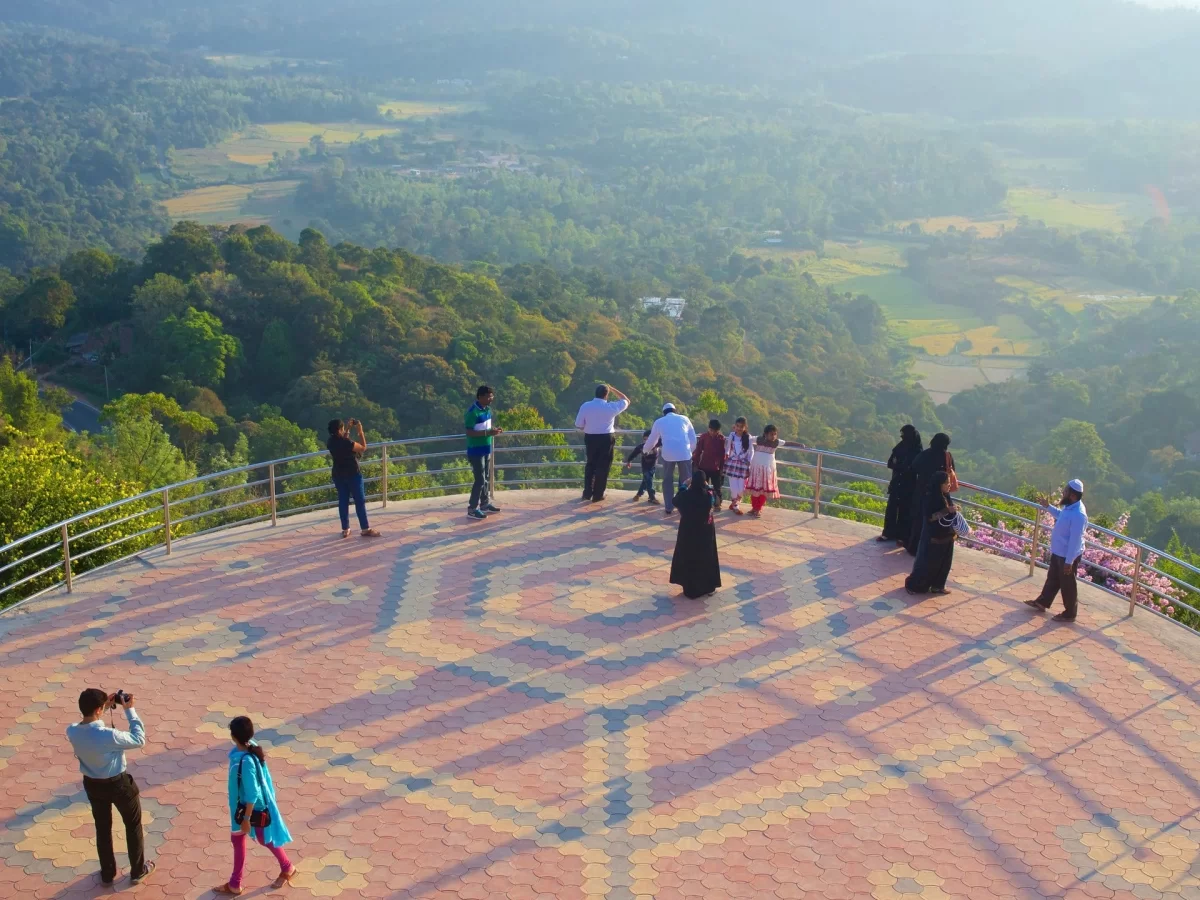 Raja Seat Garden at Madikeri Coorg during golden hour, featuring tourists viewing misty valleys, mountains, forests, perfect romantic experience Karnataka tour packages.