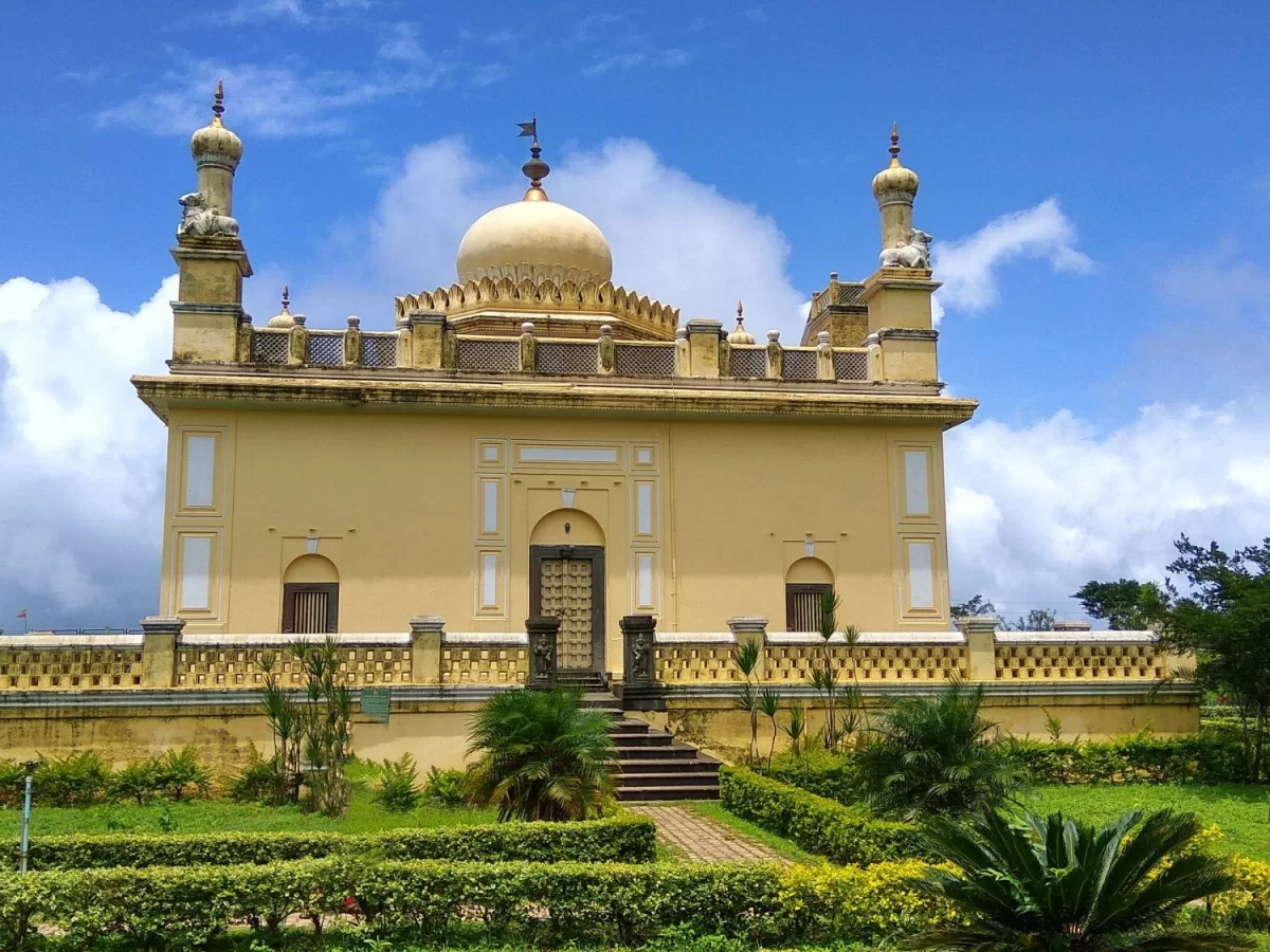 Raja's Tomb at Madikeri Coorg during sunny day, featuring yellow dome minarets, gardens, palms, flowers, perfect cultural experience Karnataka tour packages.