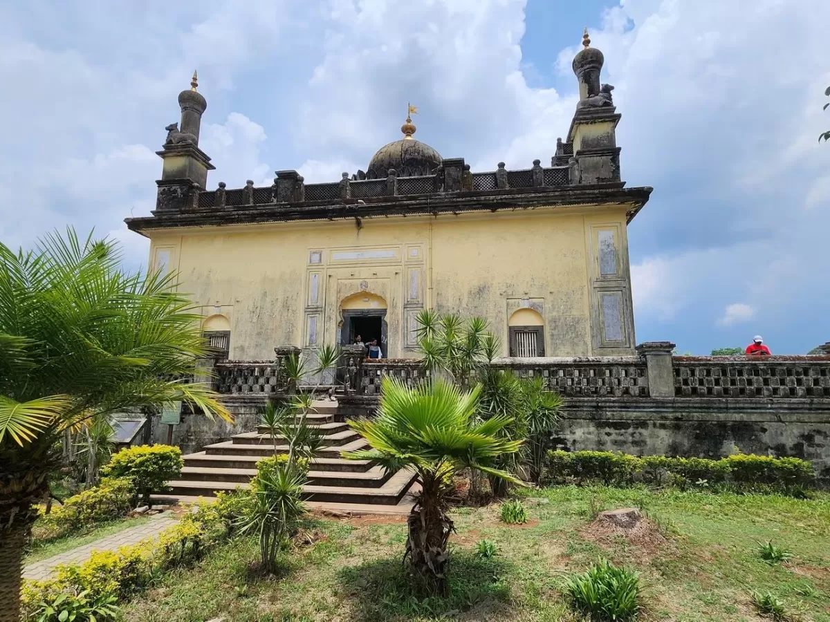 Raja's Tomb at Madikeri Coorg during partly cloudy day, featuring yellow mausoleum domes, palm trees, gardens, steps, perfect cultural experience Karnataka tour packages.