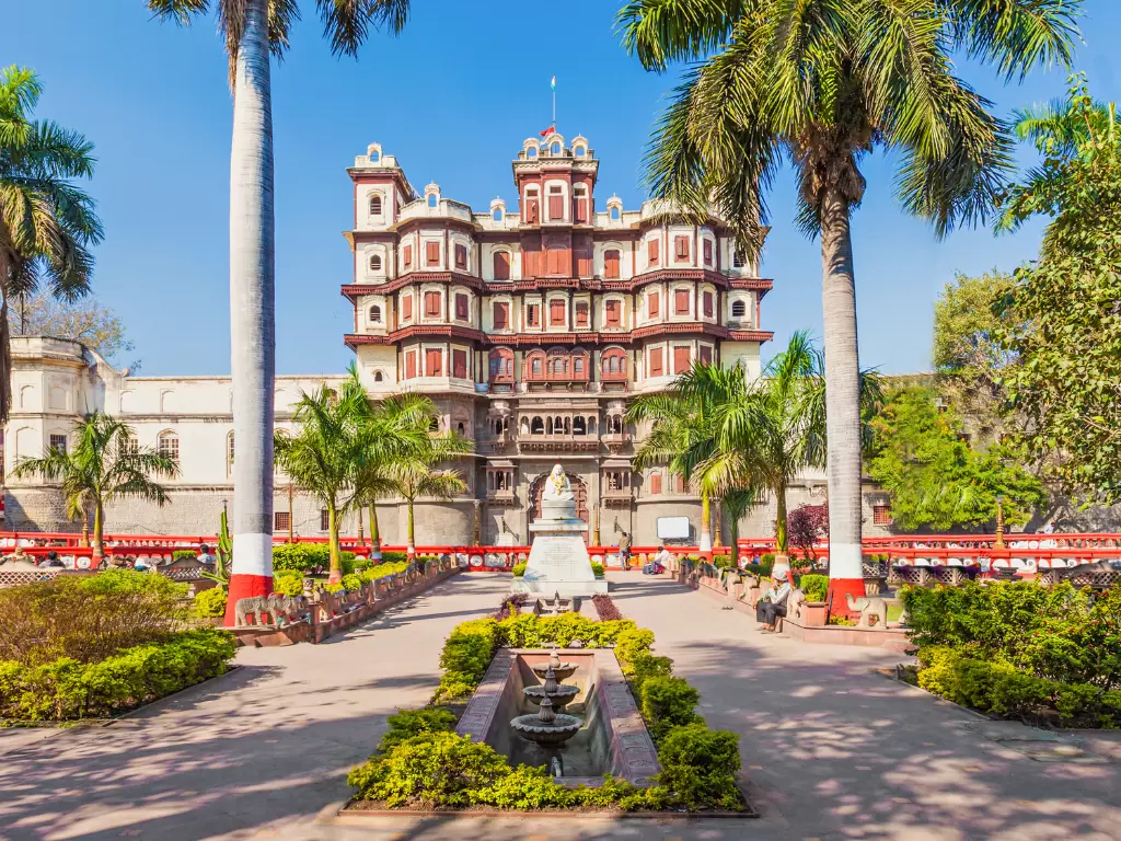 Rajwada Palace at Indore during clear daylight, featuring red-white palace palms garden fountain, perfect cultural experience Madhya Pradesh tour package.