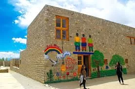 Rancho School building at Ladakh during partly cloudy skies, featuring colorful mural kids rainbow trees visitors, perfect adventure Ladakh tour package.