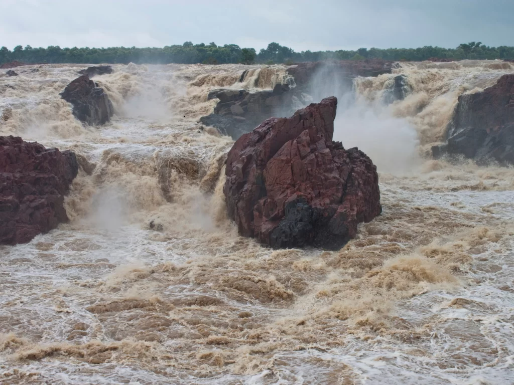 Raneh Falls near Khajuraho during monsoon season, featuring multiple cascades granite rocks Ken River mist forest backdrop, perfect Madhya Pradesh heritage nature tour package.