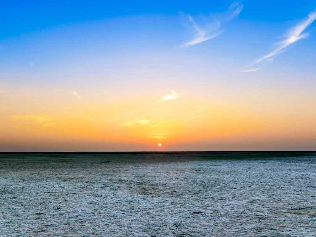 Rann of Kutch sunset during golden hour, featuring glowing sun, blue-orange skies and vast white salt desert horizon, perfect adventure experience with Gujarat tour packages.