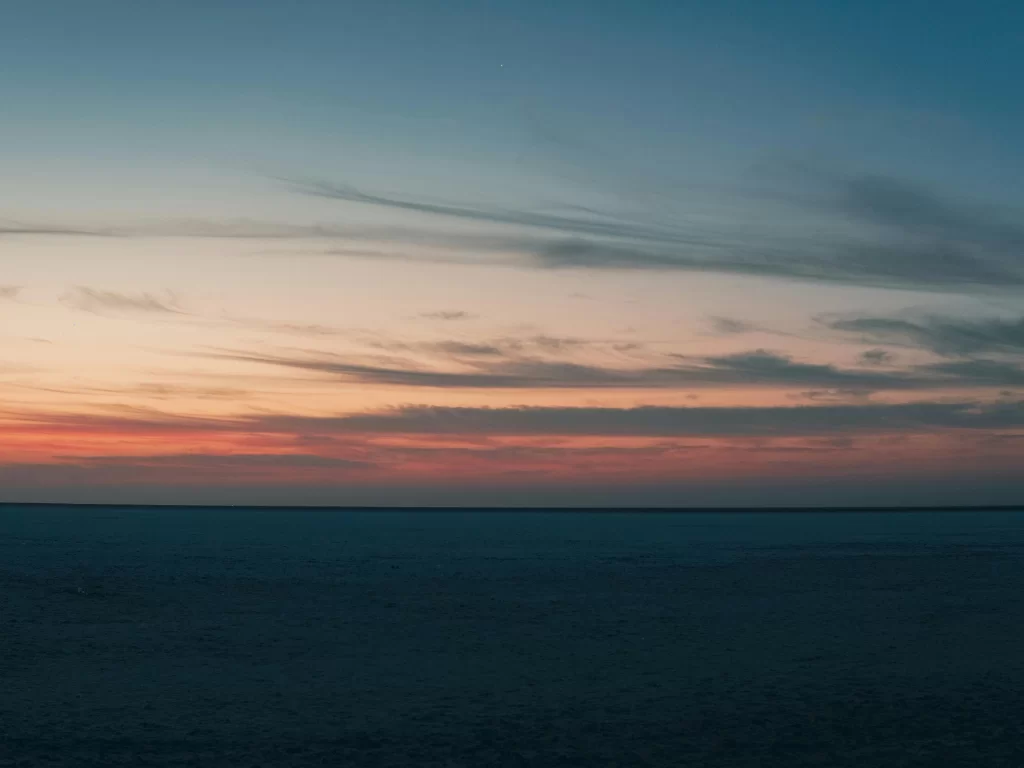 Camel cart ride at Rann of Kutch during clear day, featuring decorated yellow canopy, Kutchi man, camel and vast white salt desert, perfect adventure experience with Gujarat tour packages.