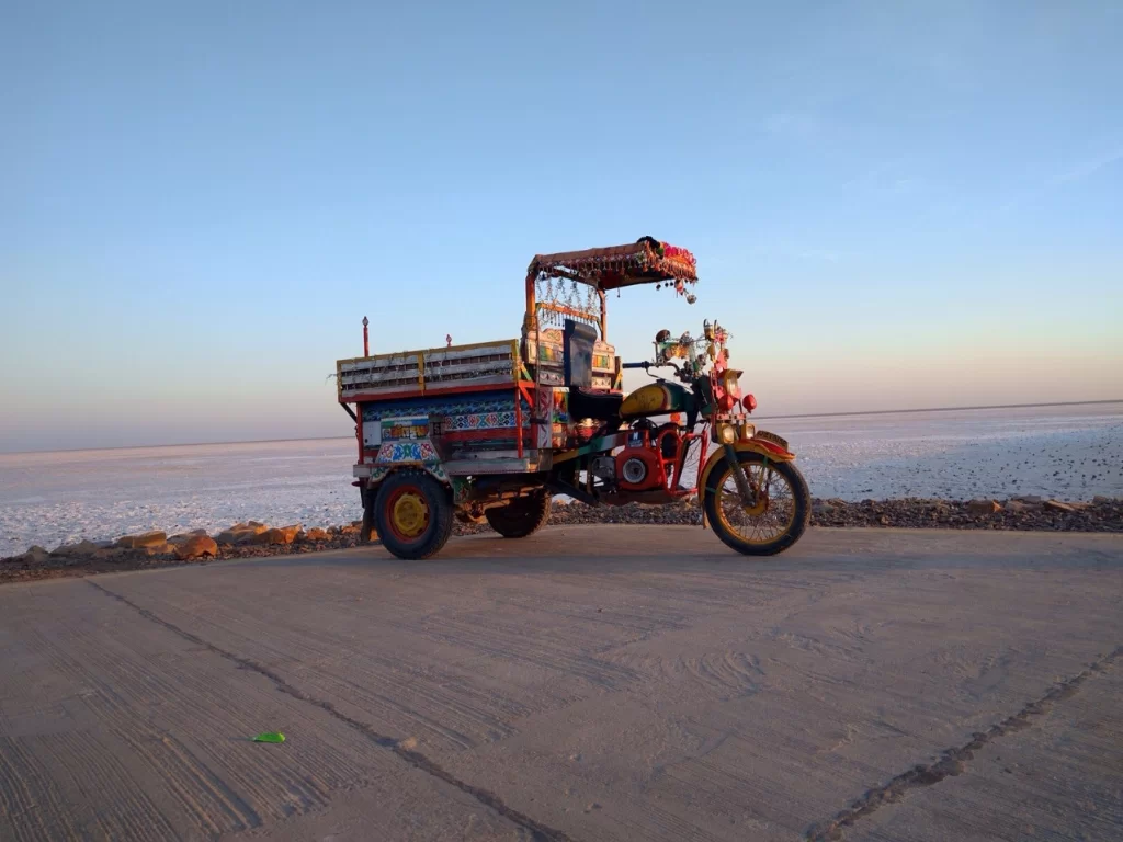 Decorated chhakda rickshaw at Rann of Kutch during golden hour, featuring colorful patterns, driver and vast white salt desert, perfect adventure experience with Gujarat tour packages.