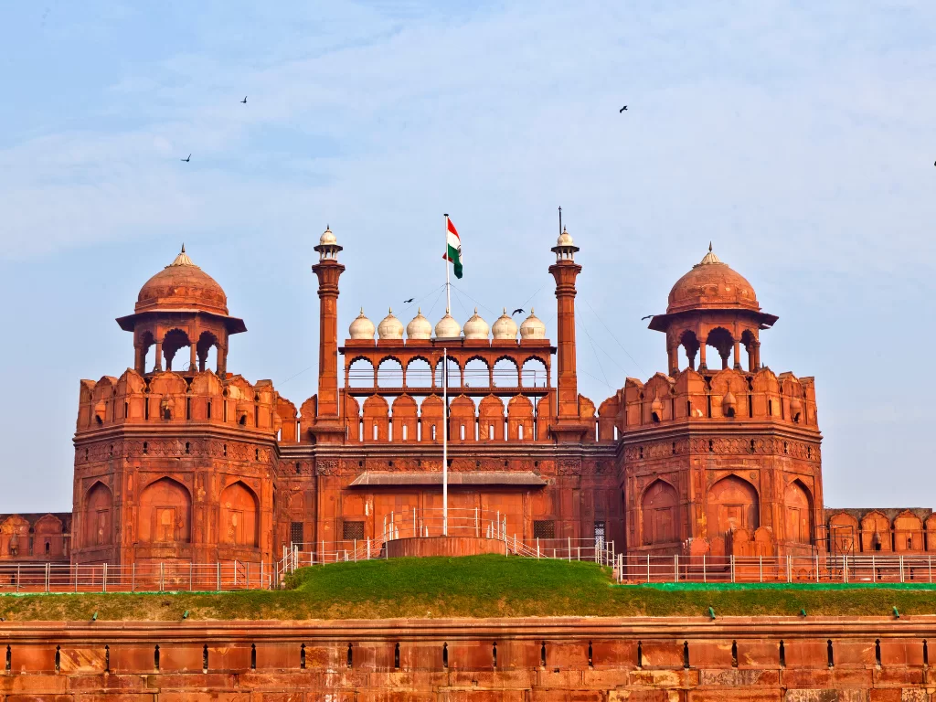 Red Fort at Delhi on clear day, featuring red sandstone walls, domes and Indian flag, perfect heritage Delhi tour package.