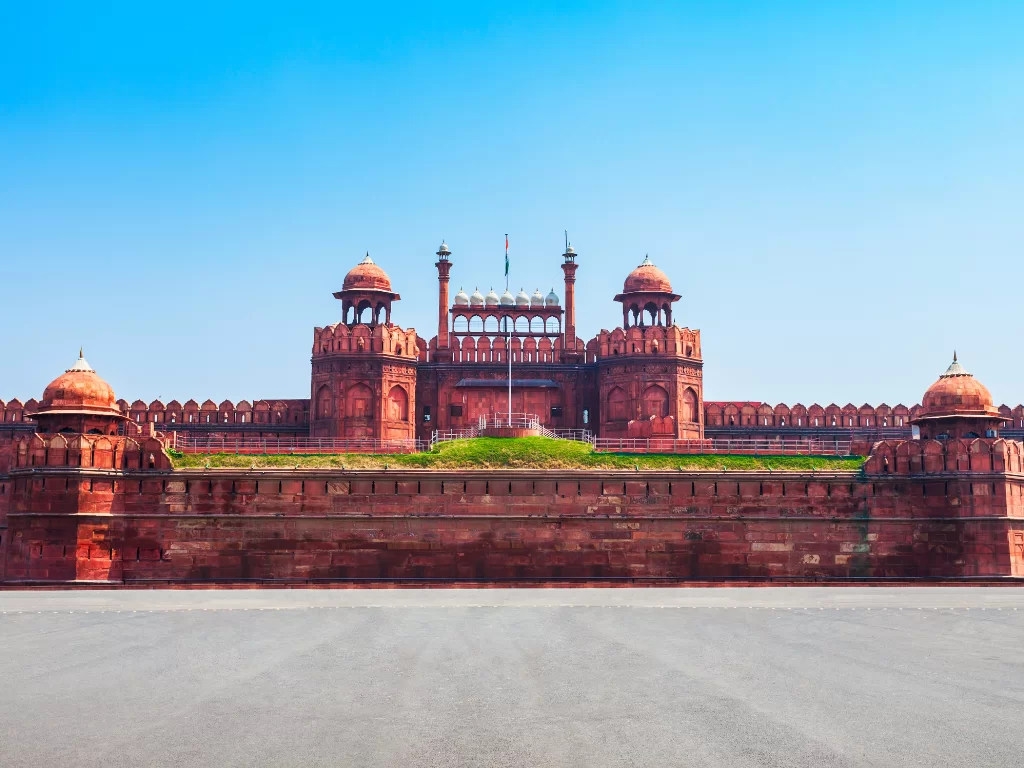 Red Fort main gate at Delhi on sunny day, featuring Indian flag and red sandstone towers, perfect heritage Delhi tour package. 