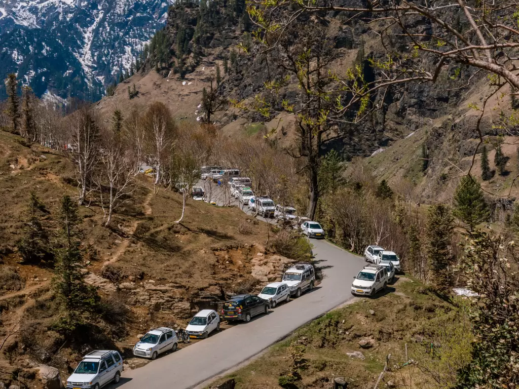 Car convoy on road at Rohtang Pass Manali during sunny weather, featuring snow-capped peaks birch trees and valley slopes, perfect adventure experience Himachal Pradesh tour package.