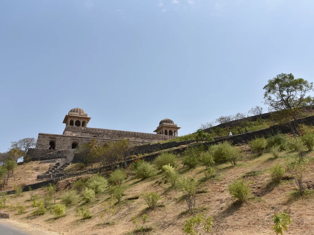 Rani Roopmati Pavilion at Gwalior Fort under clear skies, featuring domed towers amid hillside greenery, perfect heritage experience with Madhya Pradesh tour packages.