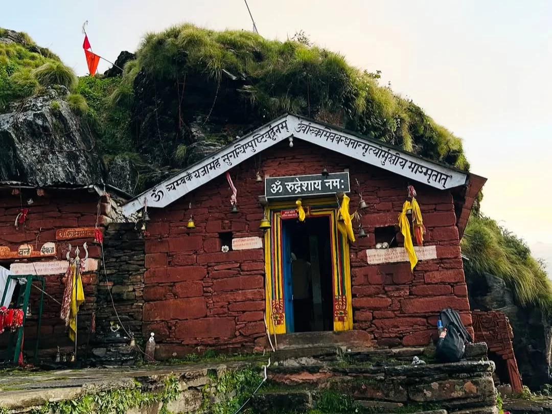 Rudranath Temple in Uttarakhand, nestled on a moss-covered rock with a vibrant yellow entrance and sacred flags—a spiritual haven in Uttarakhand tour packages.