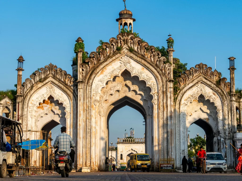 Rumi Darwaza with vines at Lucknow during sunny day, featuring ornate white arches vehicles plaza crowds, perfect cultural Uttar Pradesh tour package.