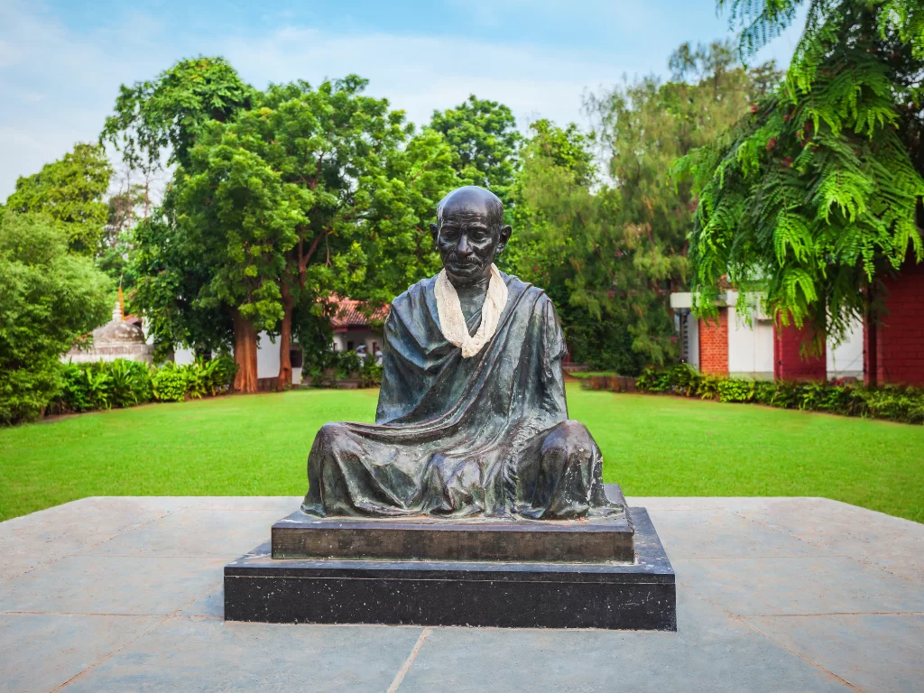 Gandhi statue at Sabarmati Ashram Ahmedabad during daylight, featuring lush gardens and trees, perfect cultural Gujarat tour package.
