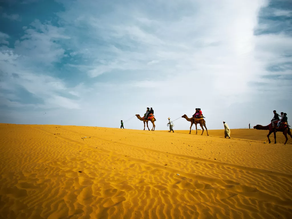 Camel safari on golden sand dunes at Sam Jaisalmer during blue hour, featuring white-robed riders and camels, perfect adventure experience in Rajasthan tour package.