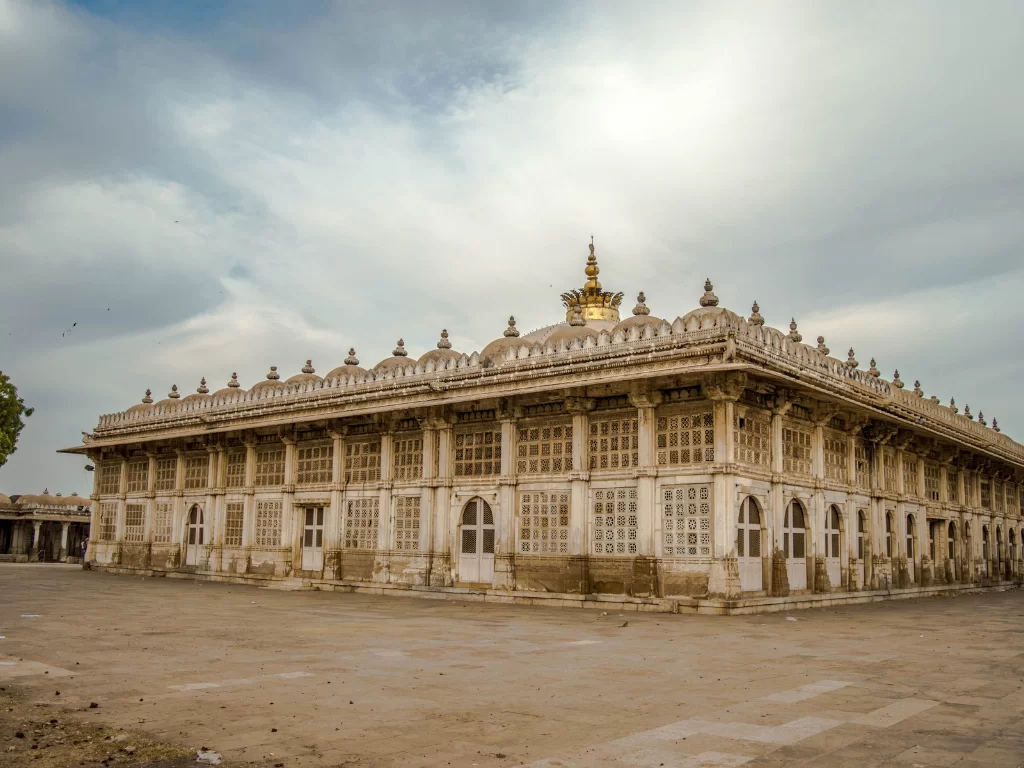 Majestic pavilion at Sarkhej Roza Ahmedabad during cloudy daylight, featuring golden dome and jali screens, perfect cultural Gujarat tour package.