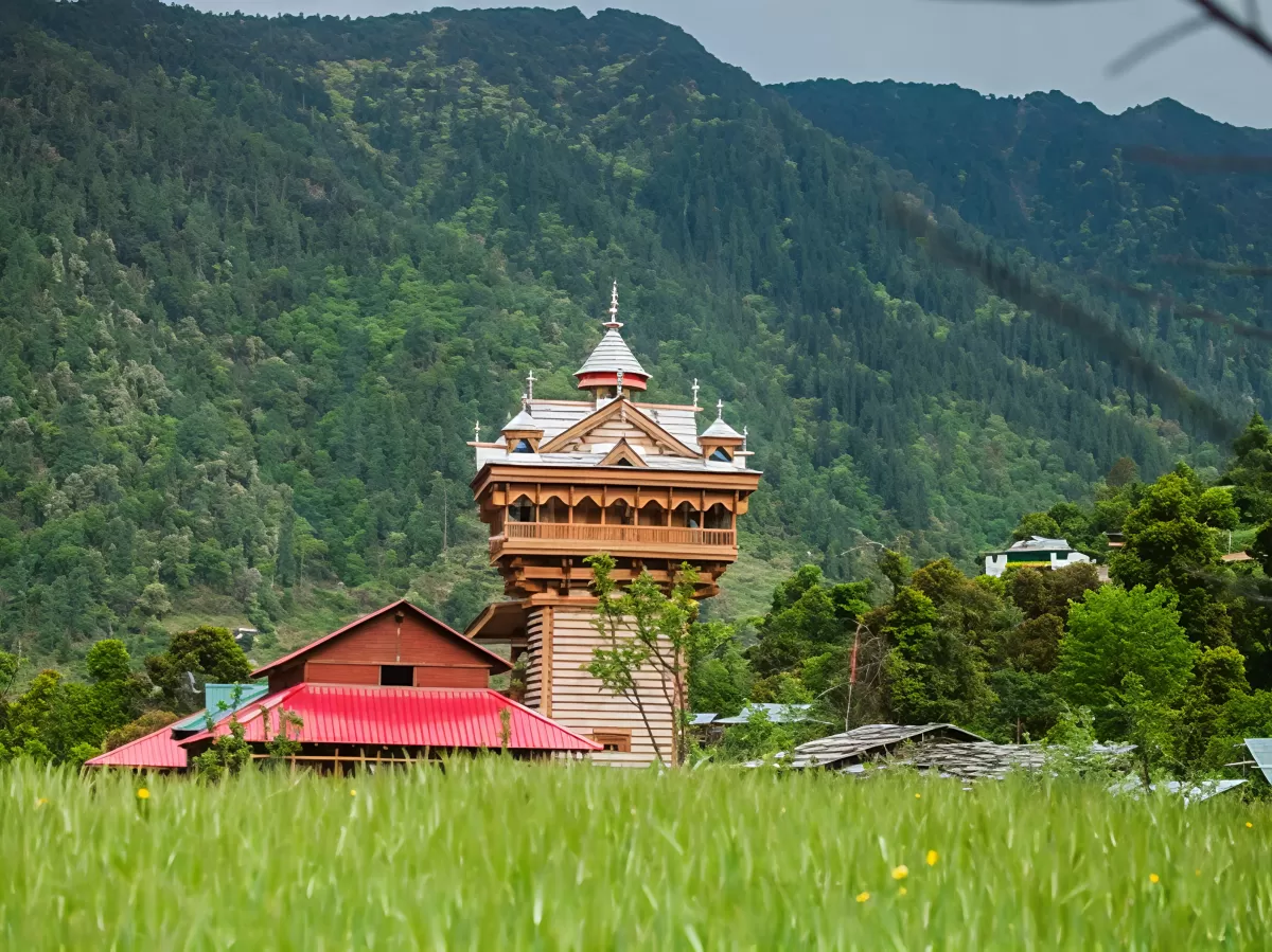 Shangchul Mahadev Temple at Shangarh Meadows Sainj Valley during cloudy weather, featuring multi-tiered wooden tower pine forests green meadows mountains, perfect adventure experience Himachal Pradesh tour package.