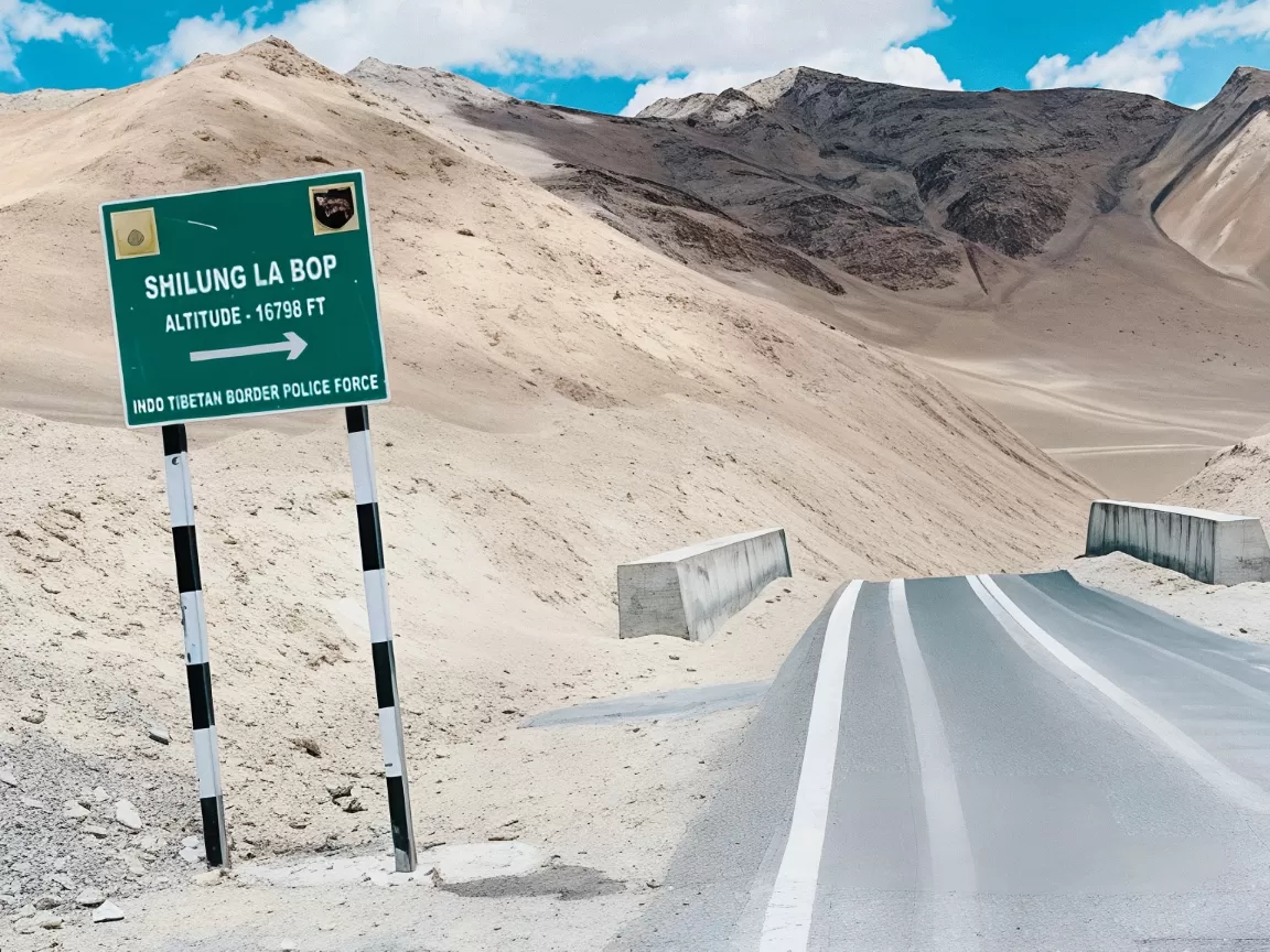 Shilung La pass signboard 17780ft Nubra-Shyok road sandy desert dunes distant mountains blue skies Ladakh India, lesser-known high-altitude BRO pass Diskit route Nubra Valley adventure drive offbeat photography spot.