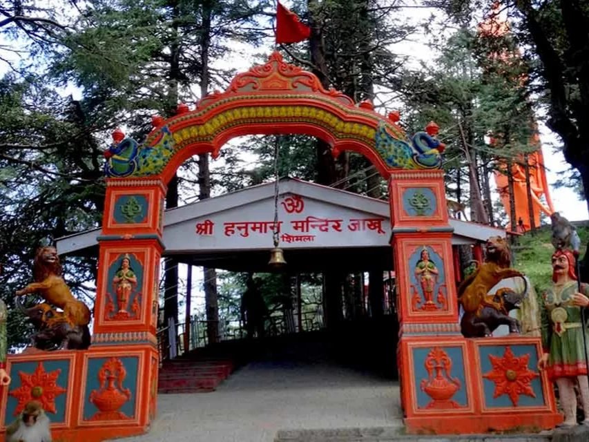 Shree Hanuman Temple at Jakhu Shimla during sunny weather, featuring ornate red gate, deodar trees, lion statues, perfect spiritual adventure, Himachal Pradesh tour packages.