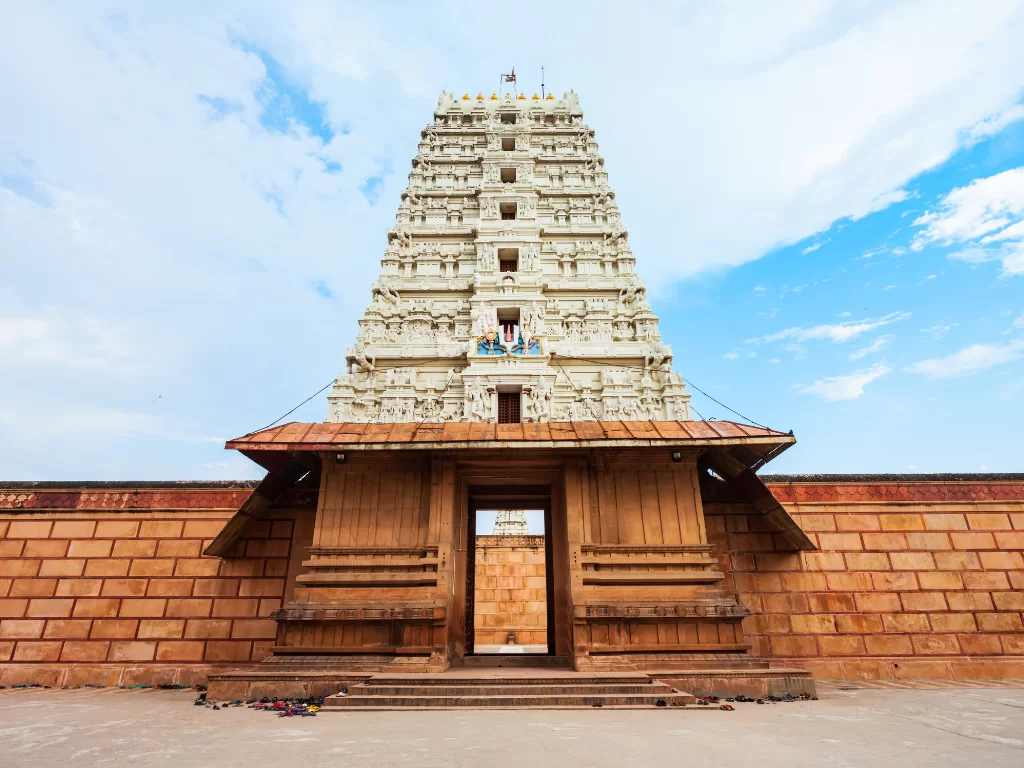 Towering gopuram of Sri Ranganathaswamy Temple during partly cloudy daytime, featuring white Dravidian architecture, wooden entrance, red sandstone walls, perfect spiritual heritage experience with Yamunotri tour package.