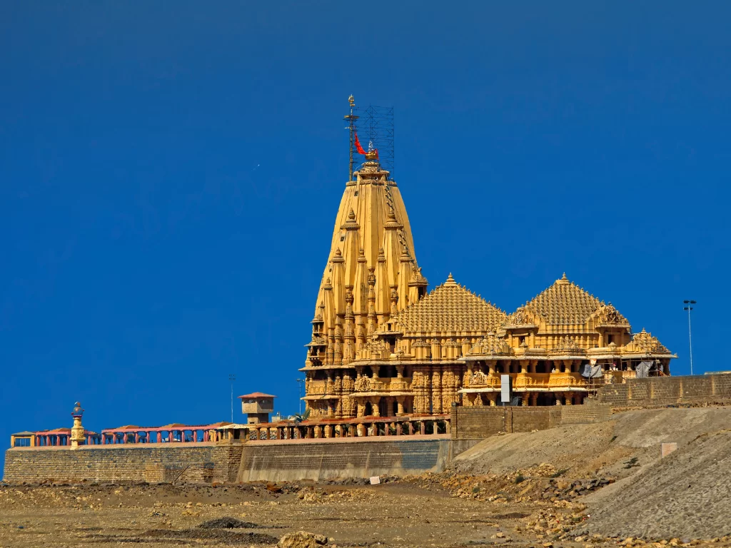 Shree Somnath Jyotirlinga Temple in Gujarat during clear day, featuring golden shikharas with saffron flag atop Chalukya-style architecture overlooking Arabian Sea and coastal embankment, perfect pilgrimage landmark with Gujarat tour packages.