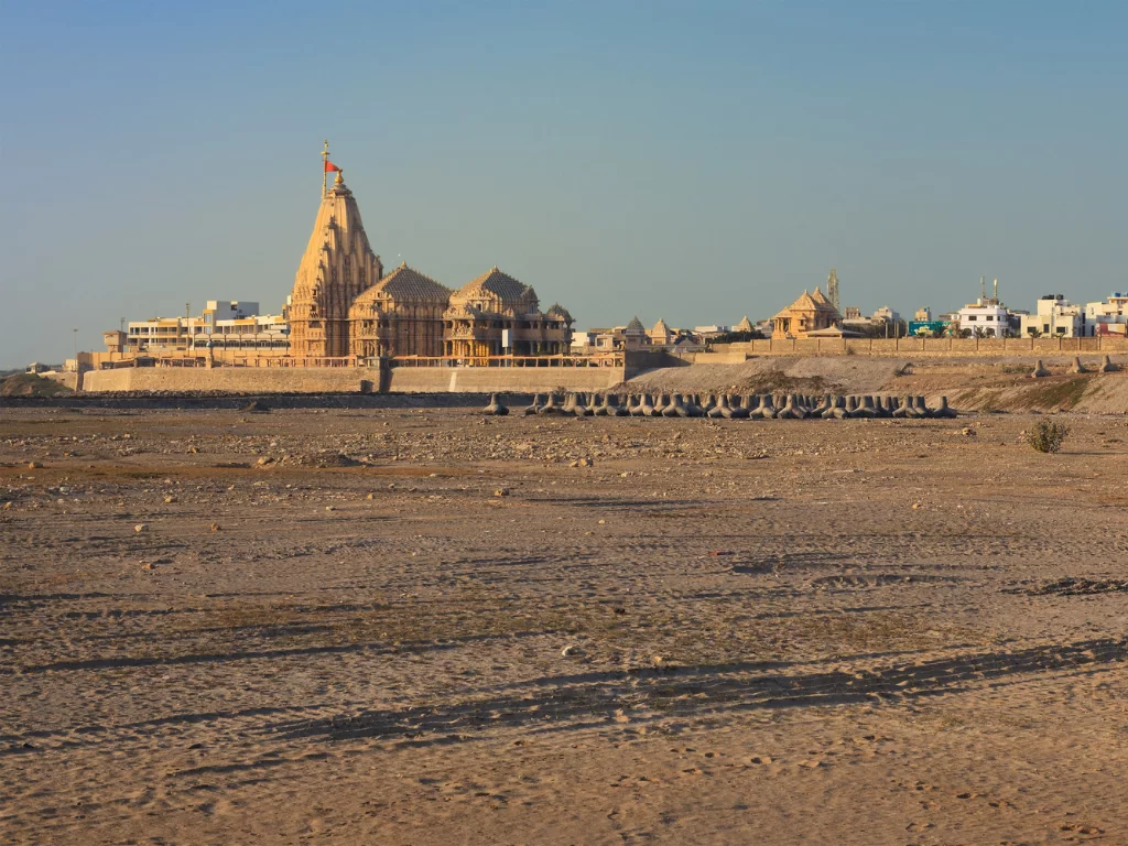 Shree Somnath Jyotirlinga Temple at Prabhas Patan during clear day, featuring shikhara with saffron flag, boundary walls, arid landscape, perfect pilgrimage experience with Gujarat tour packages.