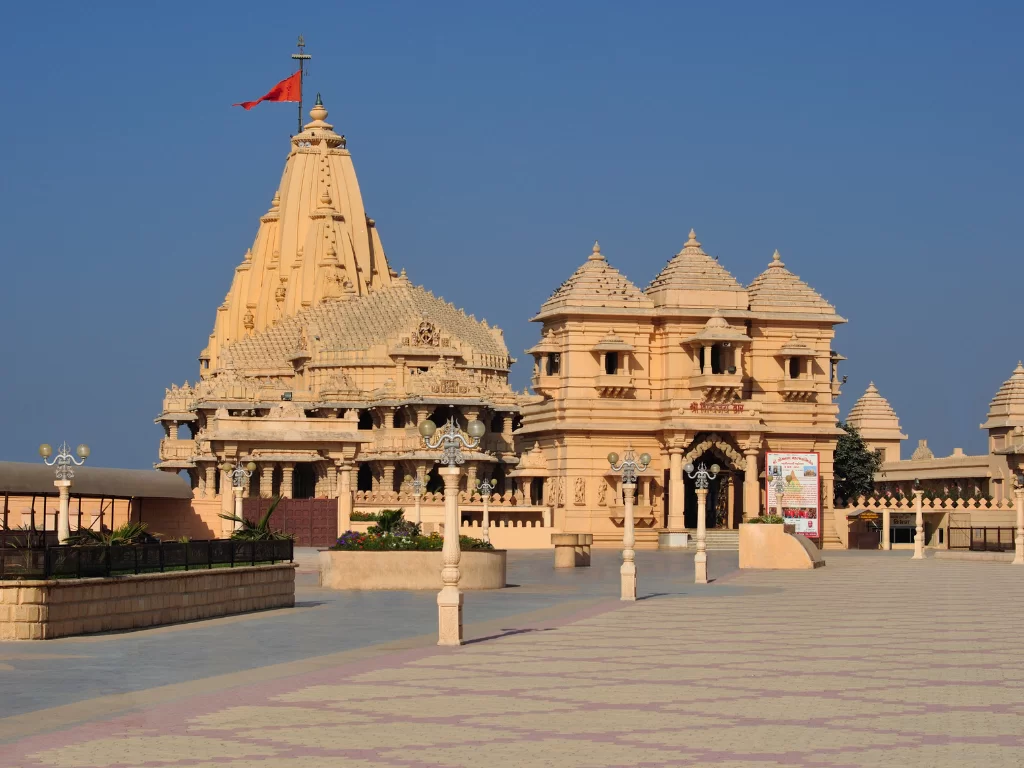 Shree Somnath Jyotirlinga Temple in Gujarat during clear day, featuring iconic Chalukya-style shikhara tower, intricate sandstone carvings, saffron flag atop spire and surrounding temple complex, perfect spiritual landmark with Gujarat tour packages.
