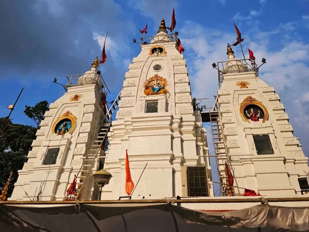 Shri Ganpati Mandir Khajrana in Indore, Madhya Pradesh, featuring three white temple spires adorned with red flags and detailed deity carvings against a blue sky, a prominent spiritual site included in Madhya Pradesh tour packages.
