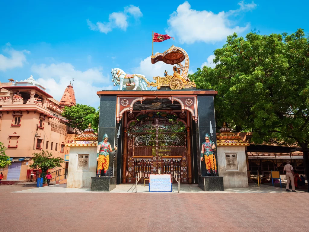 Shri Krishna Janmasthan temple main entrance Mathura Uttar Pradesh, ornate chariot gate Arjuna Krishna white horses temple domes guards trees blue skies, sacred Krishna birthplace Janmabhoomi heritage site cultural religious tourism landmark.