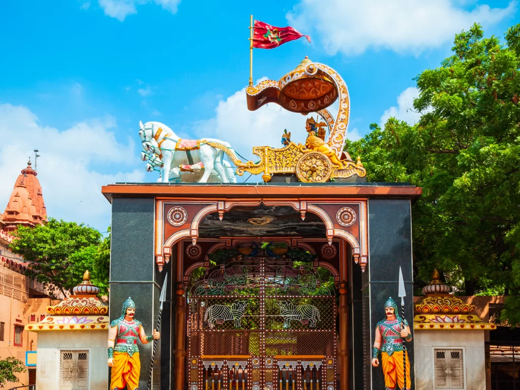 Shri Krishna Janmasthan closeup chariot gate Krishna Arjuna white horses ornate archway temple domes guards trees Mathura Uttar Pradesh, iconic Bhagavad Gita Mahabharata symbol sacred Krishna birthplace Janmabhoomi heritage attraction.
