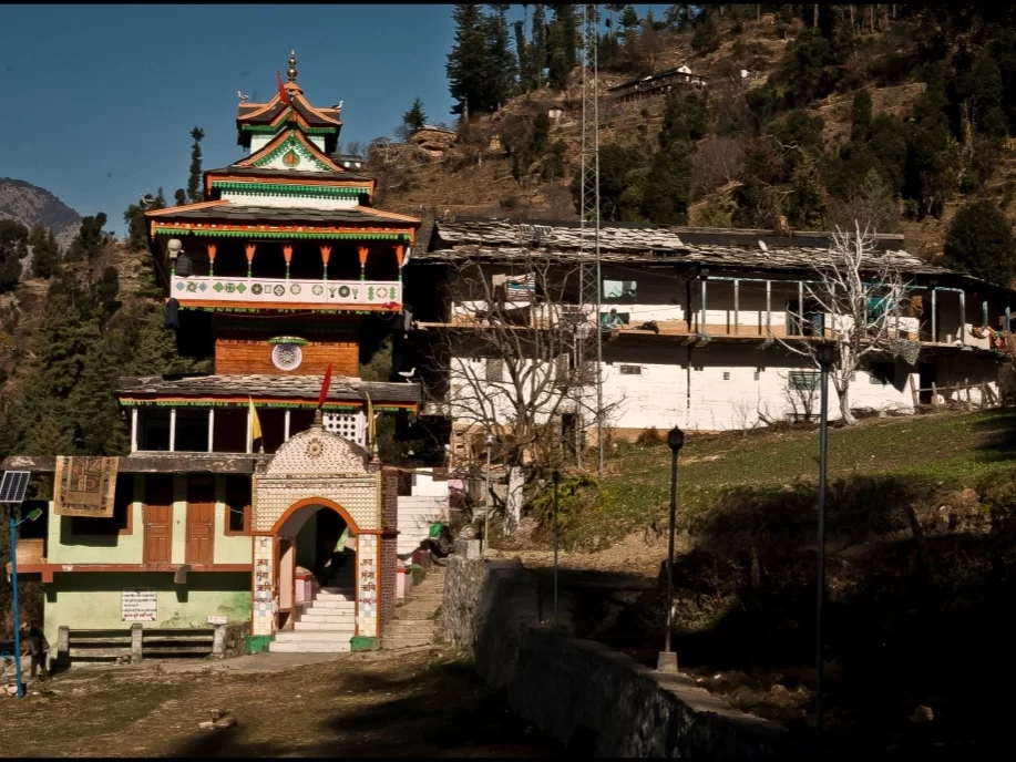 Shringa Rishi Temple in Jibhi featuring a traditional multi-tiered wooden Himachali temple with colorful carvings, arched entrance, and hillside backdrop surrounded by pine trees and village houses.