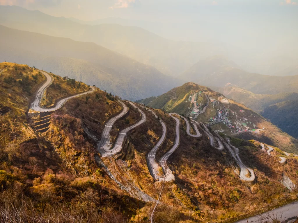 Silk Route Zuluk Sikkim during golden hour, featuring iconic zigzag hairpin bends rolling hills, perfect road trip adventure Sikkim tour package.