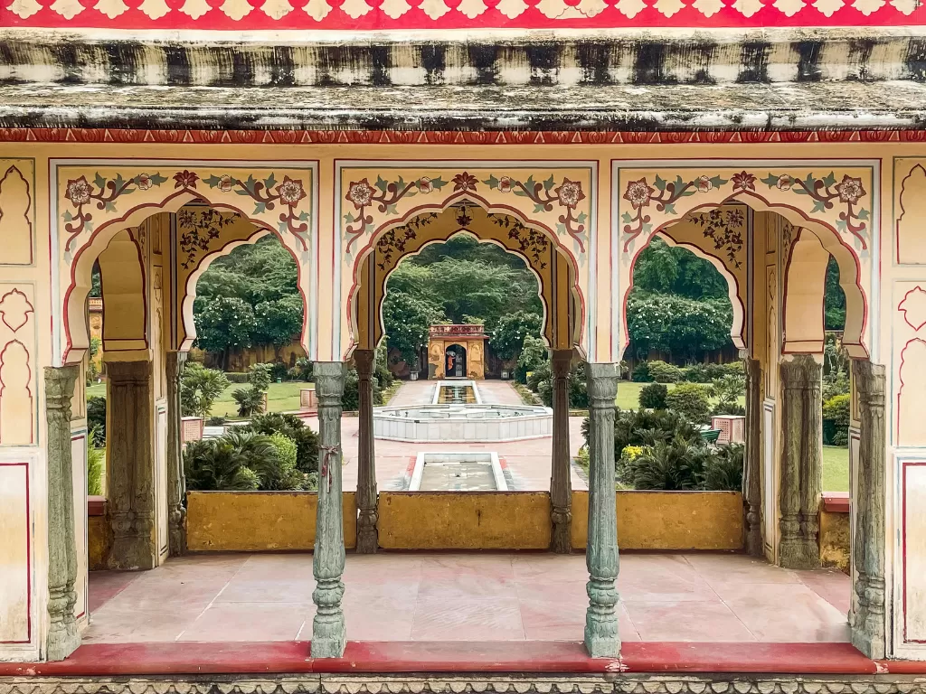 Sisodia Rani ka Bagh Jaipur ornate pink yellow arched pavilion framing central fountain garden greenery, Rajasthan Tour Packages. 