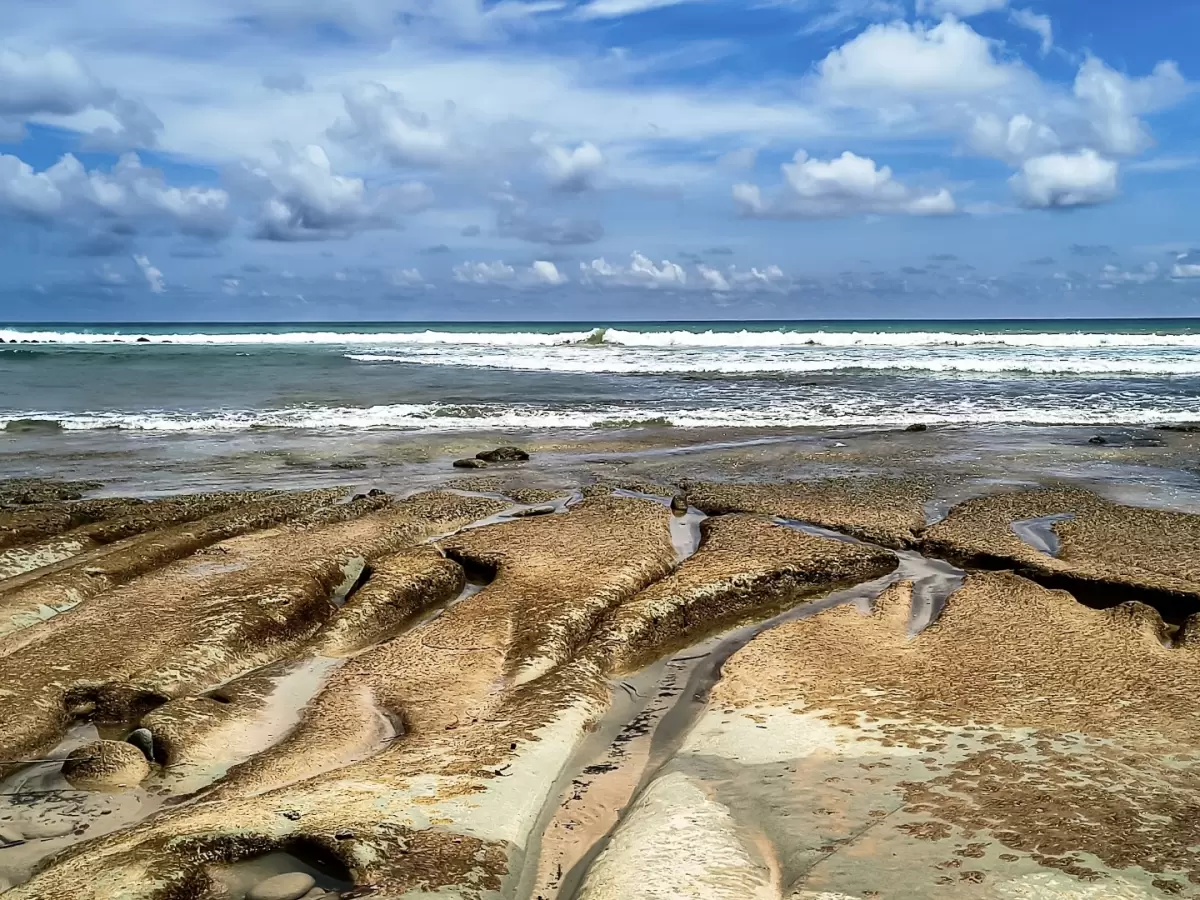 Rocky tidal flats at Sitapur Beach in Neil Island at midday, featuring textured reef and rolling waves, perfect Andaman beach tour package