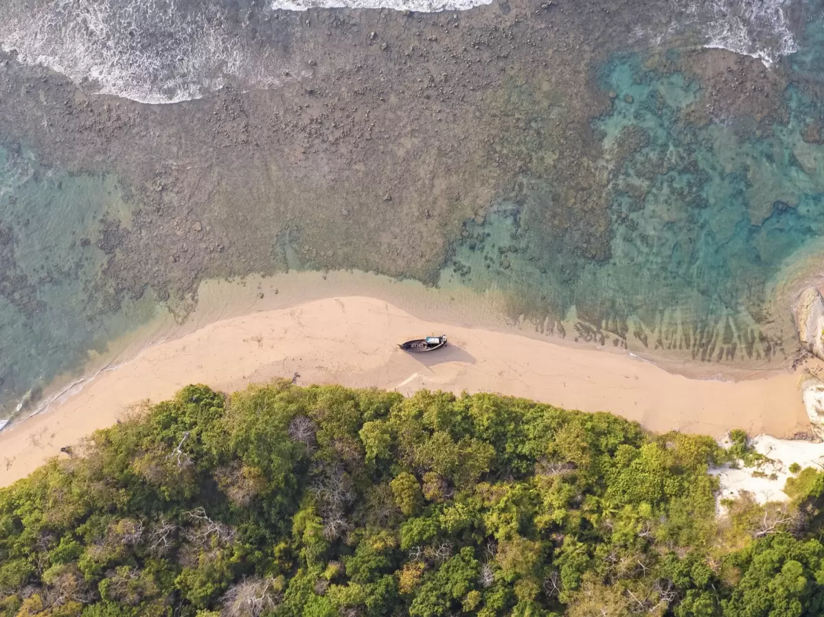 Aerial view of Sitapur Beach in Neil Island at midday, featuring sandbar, forest and beached boat, perfect Andaman beach tour package