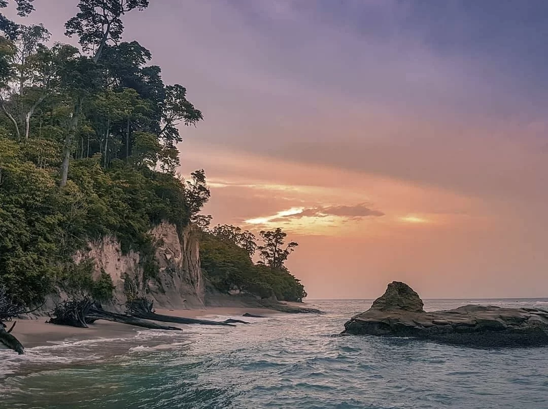 Sunset at Sitapur Beach in Neil Island, featuring rocky shoreline and forested cliffs, perfect romantic Andaman tour package