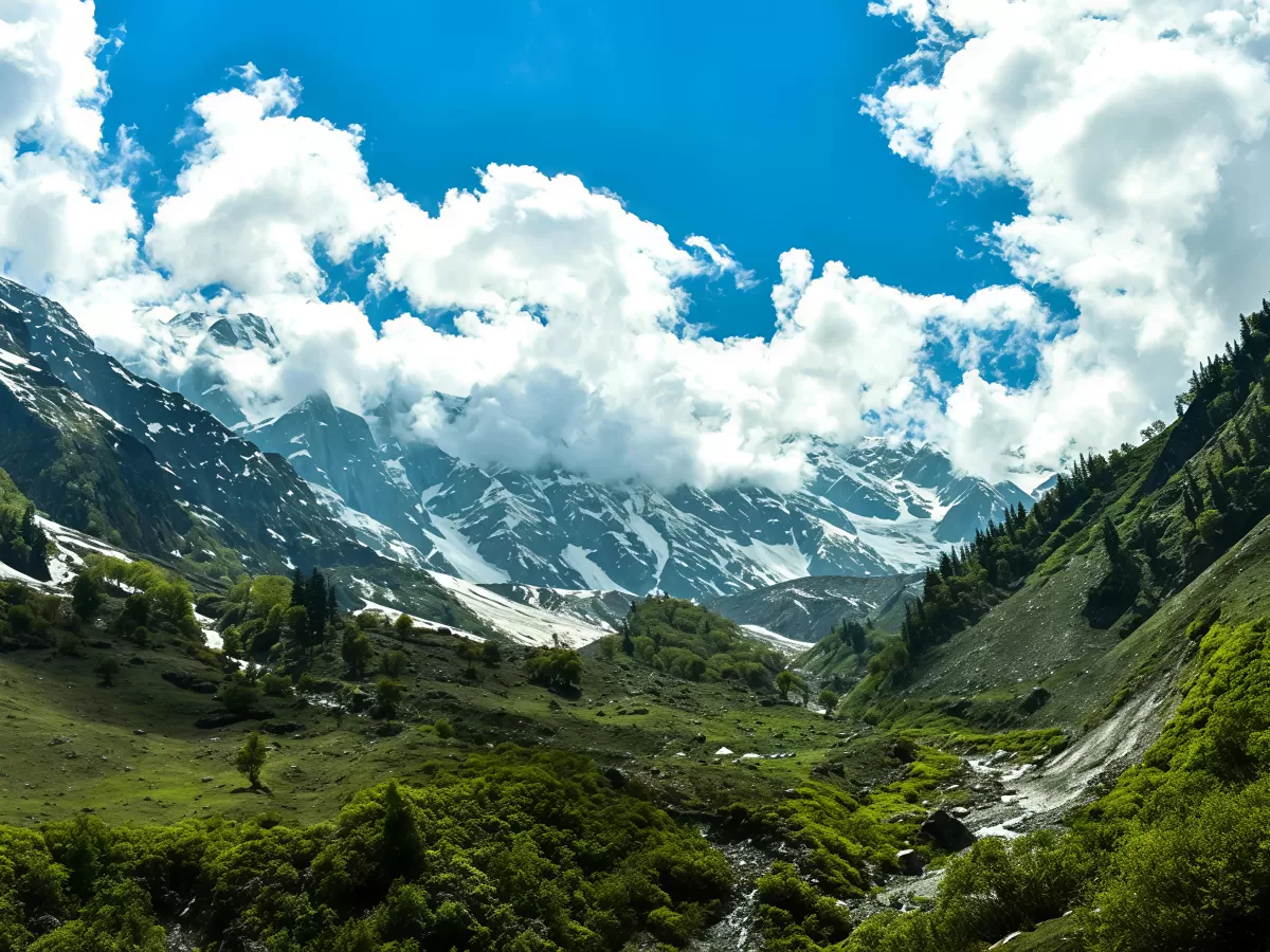Panoramic view of Solang Valley Manali during sunny skies, featuring snow peaks green meadows pine trees and clouds, perfect adventure experience Himachal Pradesh tour package.