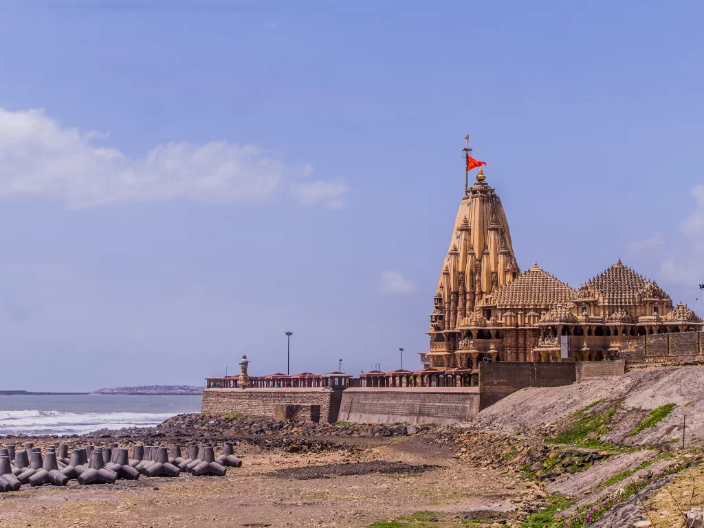 Shree Somnath Jyotirlinga Temple at Somnath Beach during clear day, featuring shikhara with saffron flag, sea waves, breakwaters, perfect pilgrimage experience with Gujarat tour packages.