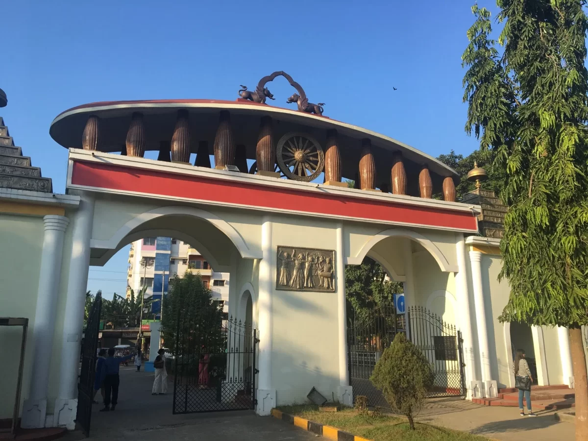 main gate at Srimanta Sankardev Kalakshetra Guwahati during sunny day, featuring Assamese motifs wheel dragons trees, perfect cultural experience Assam tour package.