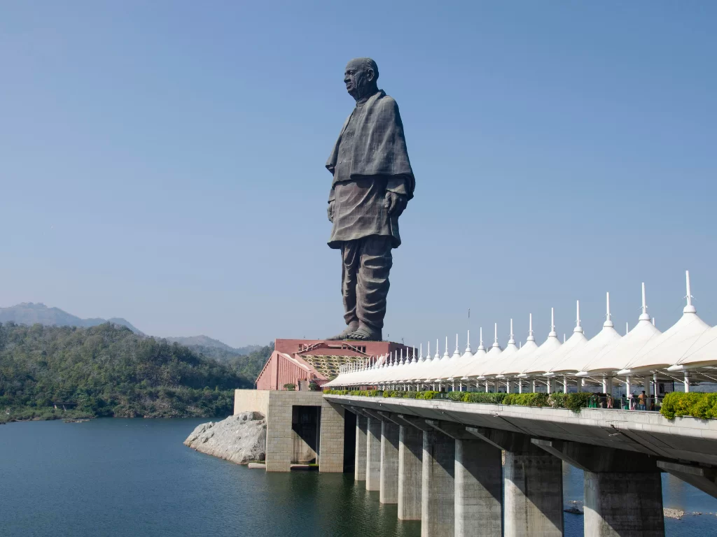 Statue of Unity in Gujarat during clear day, featuring 182m tall Sardar Patel bronze statue, connecting bridge with white canopies, Narmada River and surrounding hills, perfect cultural landmark with Gujarat tour packages.