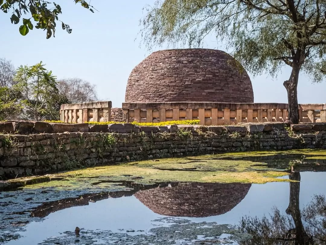 Stupa No. 2 at Sanchi in Madhya Pradesh with ancient brick dome and stone railing reflected in water, featured in Madhya Pradesh tour packages