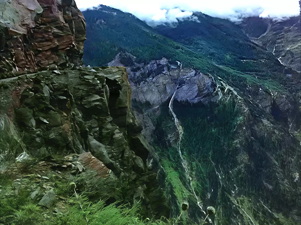 Suicide Point Kalpa Kinnaur during cloudy skies, featuring sheer red rock cliff forested deep valley cascading stream pine covered mountains, perfect thrilling viewpoint Himachal Pradesh tour package.