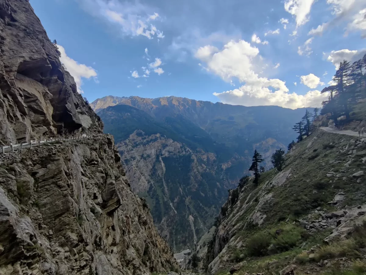 Suicide Point Kalpa Kinnaur during partly cloudy skies, featuring hairpin bend road cliff drop lush green forested valley snow mountains, perfect adventure viewpoint Himachal Pradesh tour package.