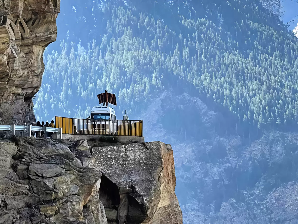 Suicide Point Kalpa Kinnaur during clear skies, featuring roadside viewing platform bus barriers people dramatic cliff drop forested valley snow mountains, perfect adventure viewpoint Himachal Pradesh tour package.