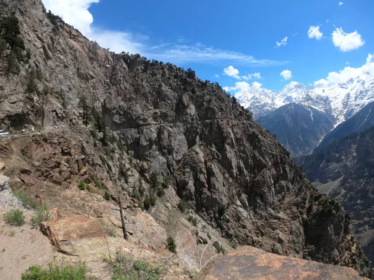 Suicide Point Kalpa Kinnaur during clear blue skies, featuring dramatic cliff drop Hindustan Tibet Road hairpin bends barren mountains pine trees snow peaks, perfect adventure viewpoint Himachal Pradesh tour package.