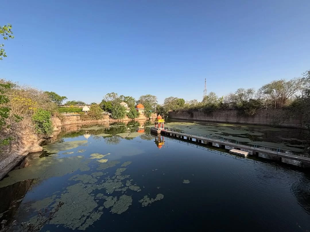 Suraj Kund in Gwalior featuring a historic stepped reservoir with calm water, surrounding stone walls, and a small shrine pavilion, a heritage attraction included in Madhya Pradesh tour packages