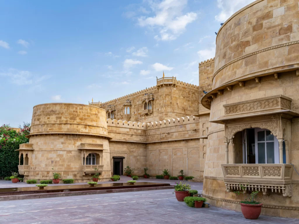 Majestic towers at Suryagarh Palace Jaisalmer during clear sky, featuring sandstone jharokhas, balconies and potted plants, perfect romantic experience in Rajasthan tour package.