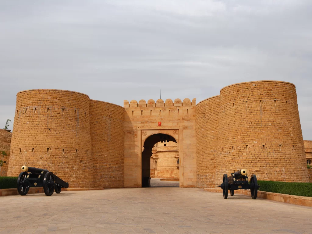 Imposing gateway at Suryagarh Palace Jaisalmer during sunny afternoon, featuring sandstone towers, cannons and arches, perfect romantic experience in Rajasthan tour package.